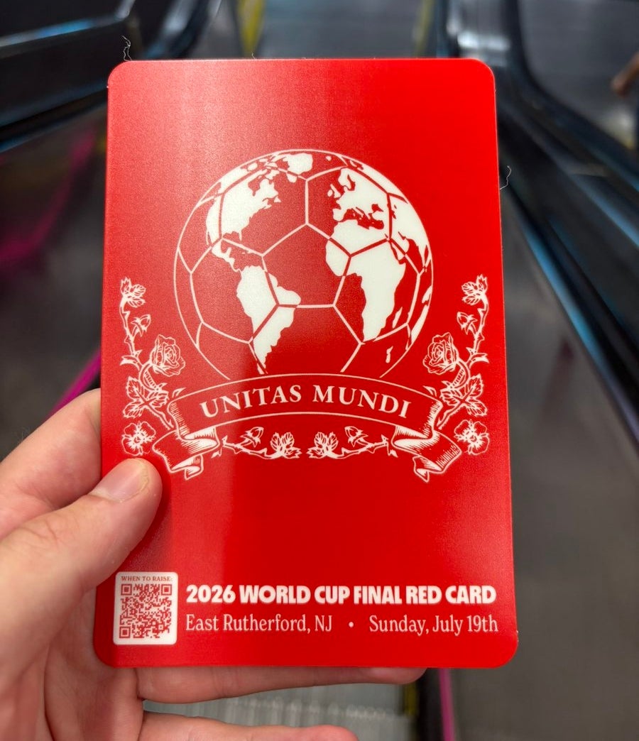 Hand holding a red card with "2026 World Cup Final Red Card" and details, featuring a globe shaped like a soccer ball with "Unitas Mundi" below it