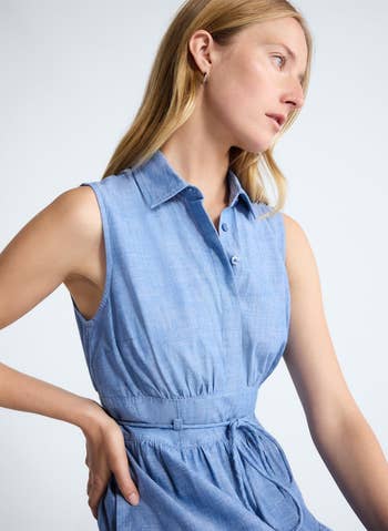 Person in a sleeveless, belted chambray dress looks to the side; focus on casual style