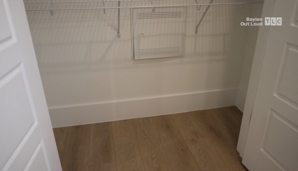 A double-doored primary suite closet opens to builder-grade wire shelving floating above wood-toned flooring.
