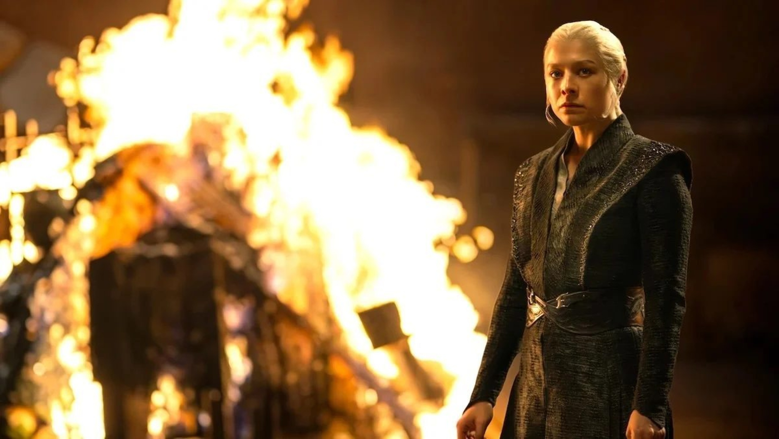 Rhaenya at night stands off to the side in front of a raging fire on House of the Dragon