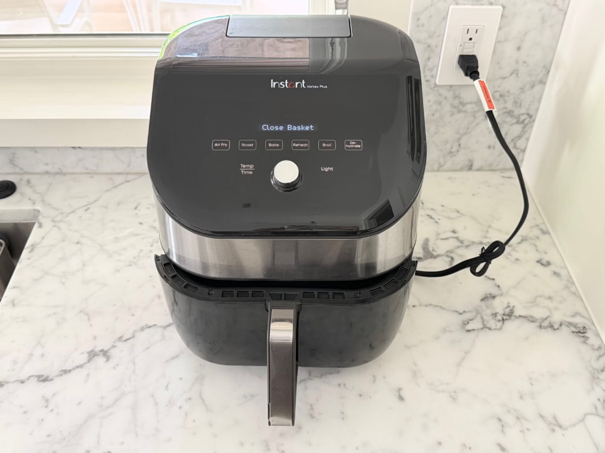 Instant Vortex Plus air fryer sits plugged in on a marble countertop with its display reading