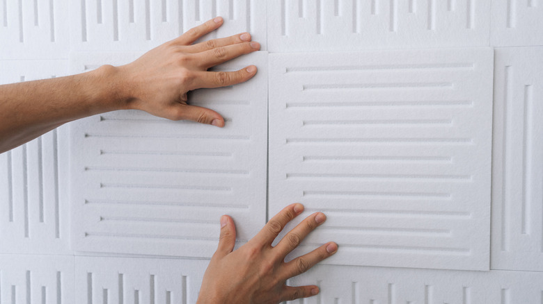 Two hands securing white acoustic panels to a wall.