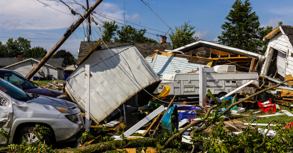 Destructive tornado damage to a house, car, and trailer in a residential neighborhood.