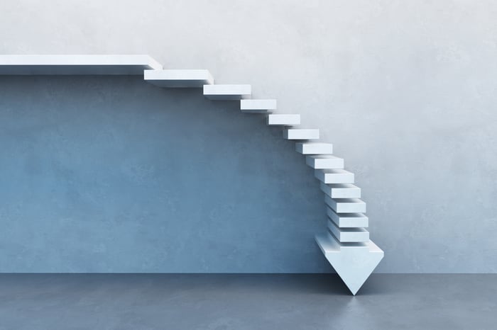 White stairs form an arrow pointing down, set against the backdrop of a gray wall.