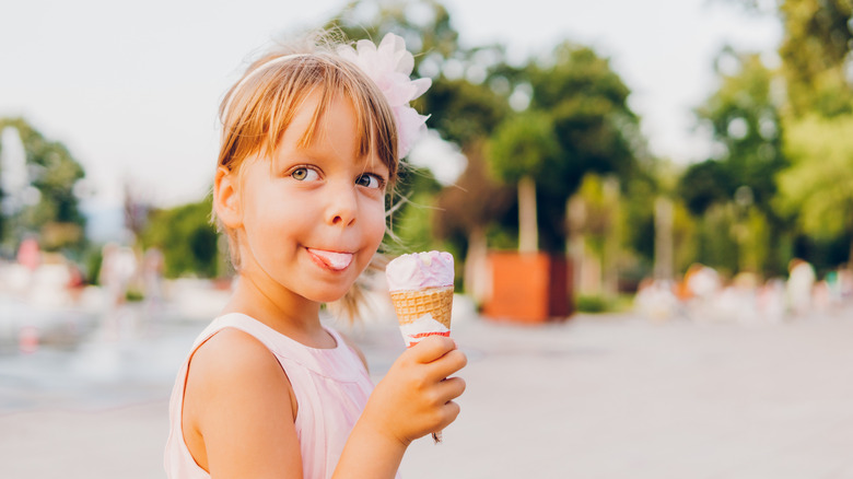 A beautiful little girl in a pink dress eating ice cream at a park.