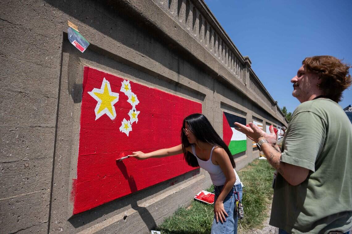 Volunteers Allison Muzzi and John Brant paint the flag of China as part of a series of flag murals on Van Brunt Boulevard in Kansas City, on Monday, July 20, 2026. When complete, the mural will feature more than 100 flags representing the demographics of the neighborhood.