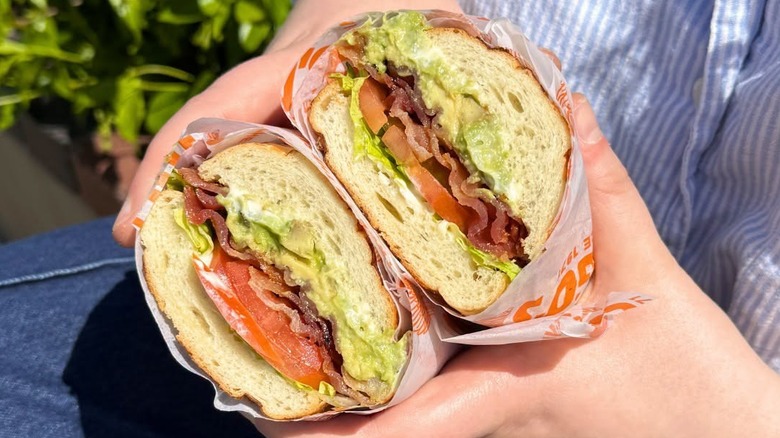 Hand's holding halved Togo's sandwich with bacon, lettuce, tomato, avocado, and mayo