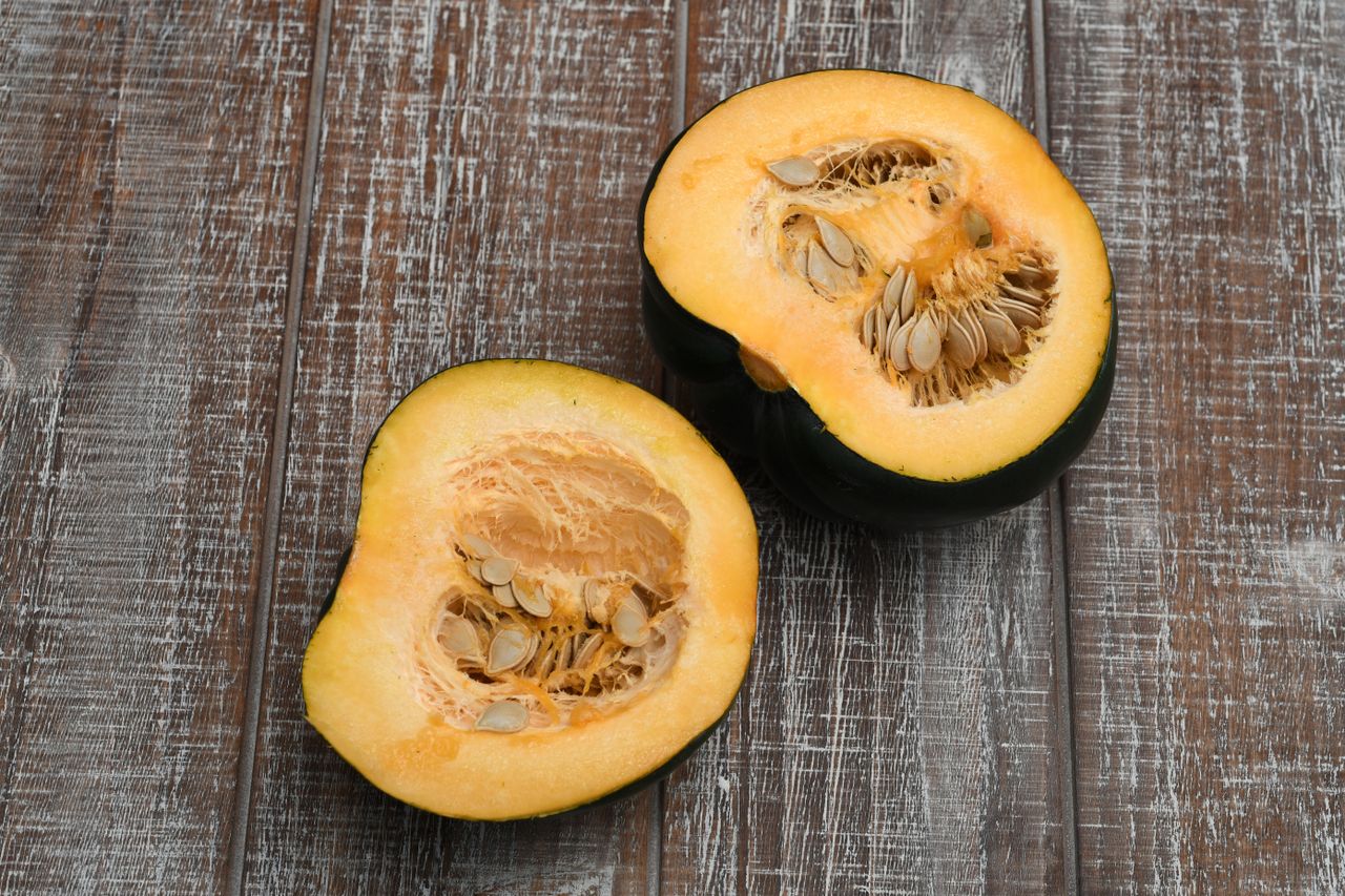 A halved acorn squash with visible seeds displayed on a wooden surface