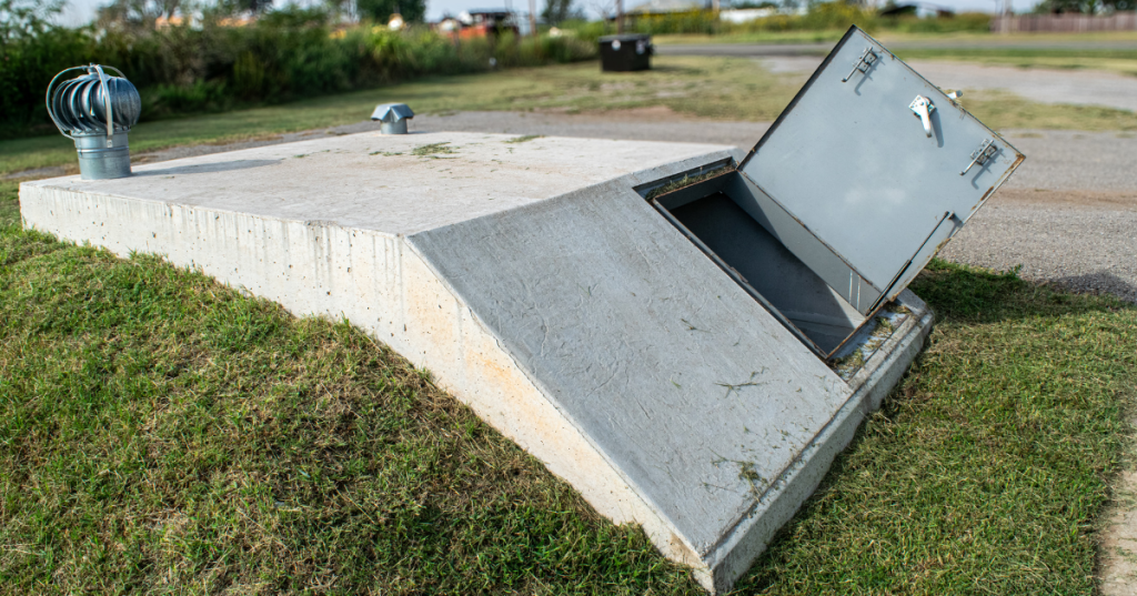 Concrete underground tornado storm shelter with an open heavy door for safety.