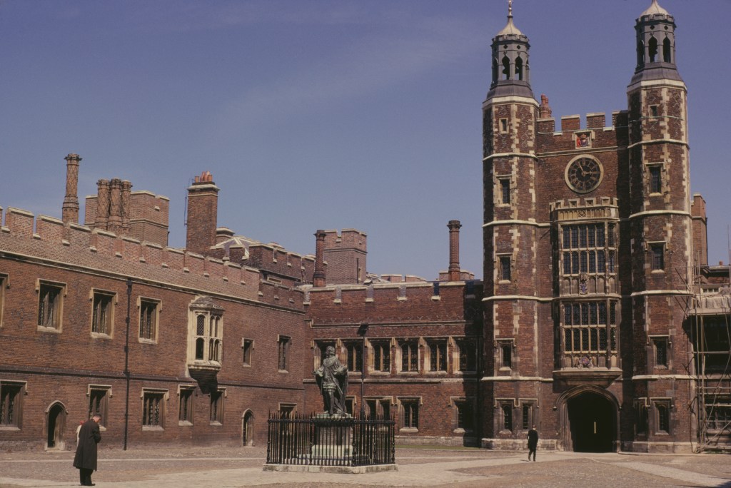 Eton College courtyard with a statue, clock tower, and two men.
