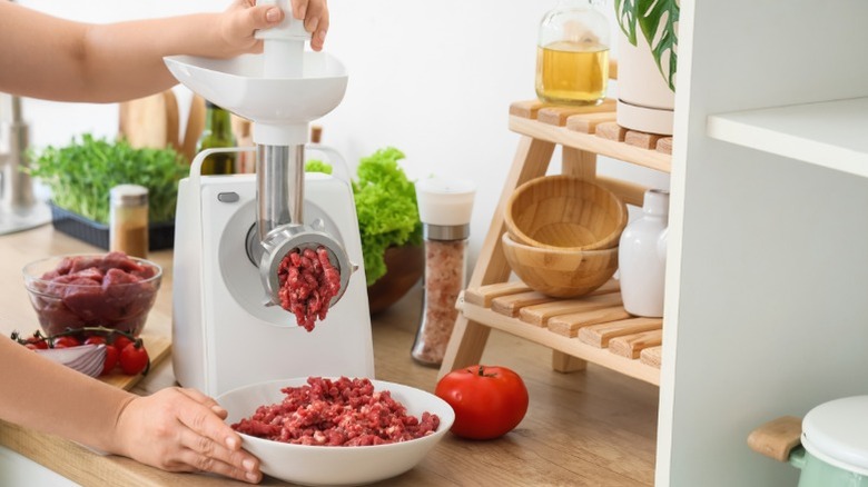 A person using a meat grinder in a modern kitchen.