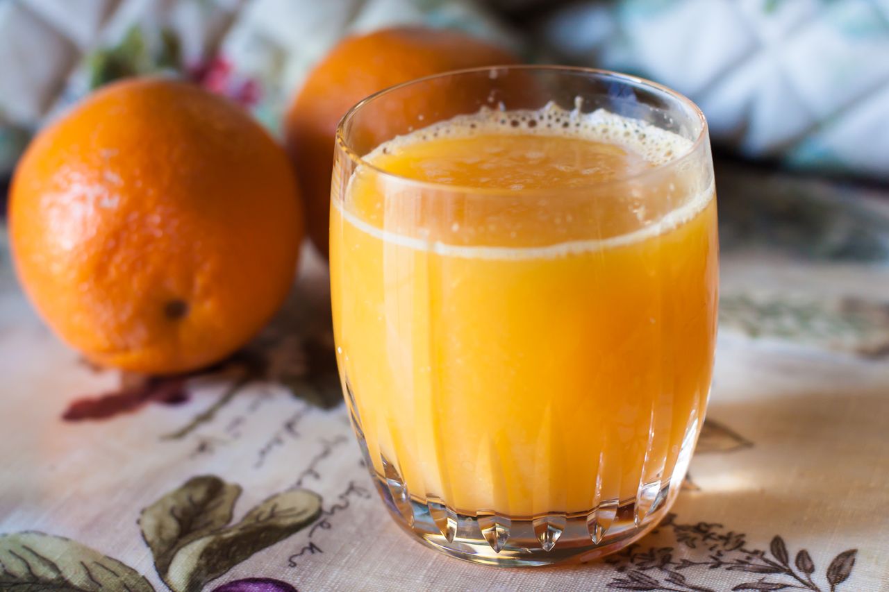 Glass of orange juice next to two whole oranges on a table