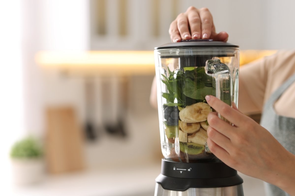 A person is holding a blender full of ingredients for a smoothie.