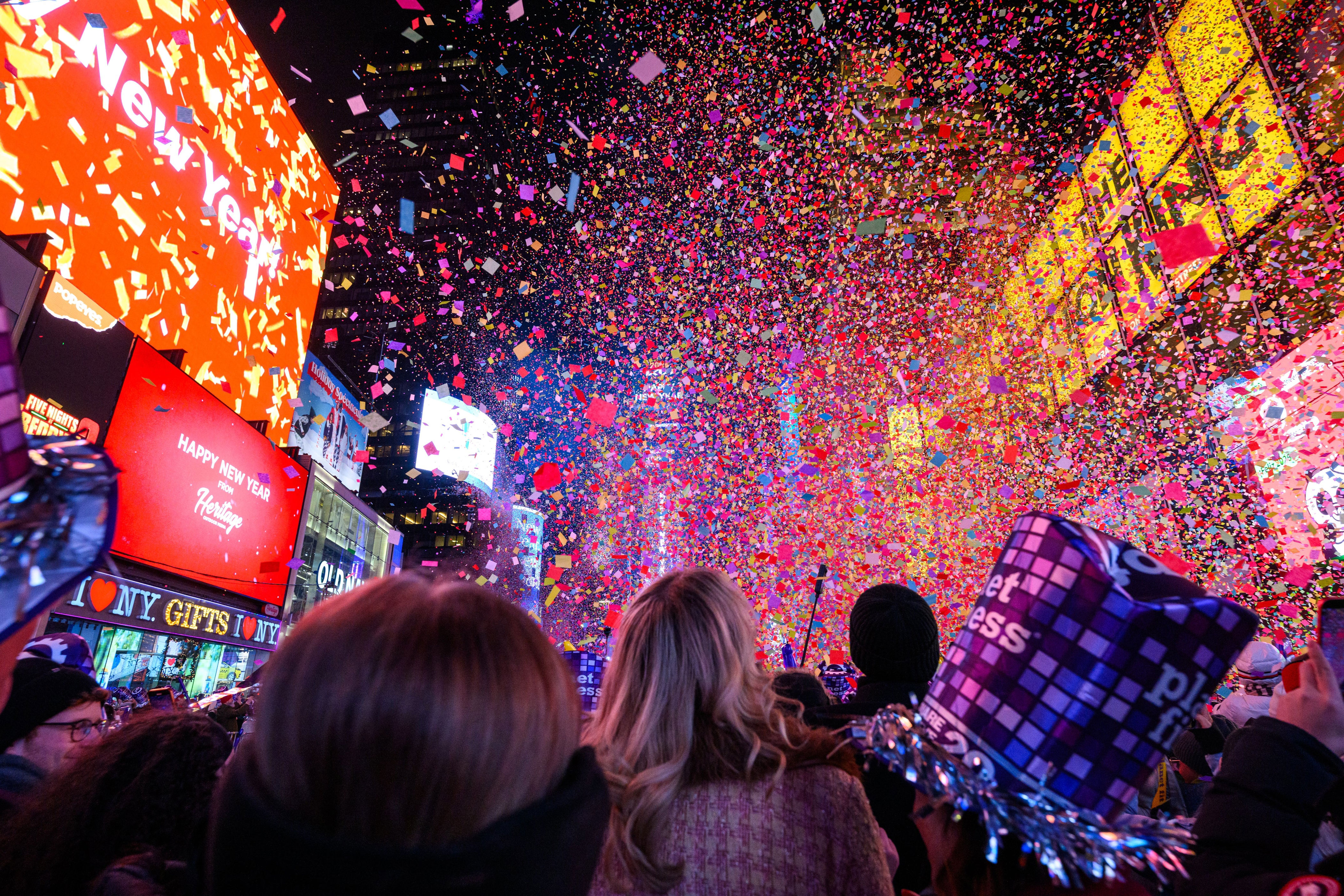 A crowd in Times Square watches colorful confetti falling during a festive celebration, surrounded by bright digital billboards