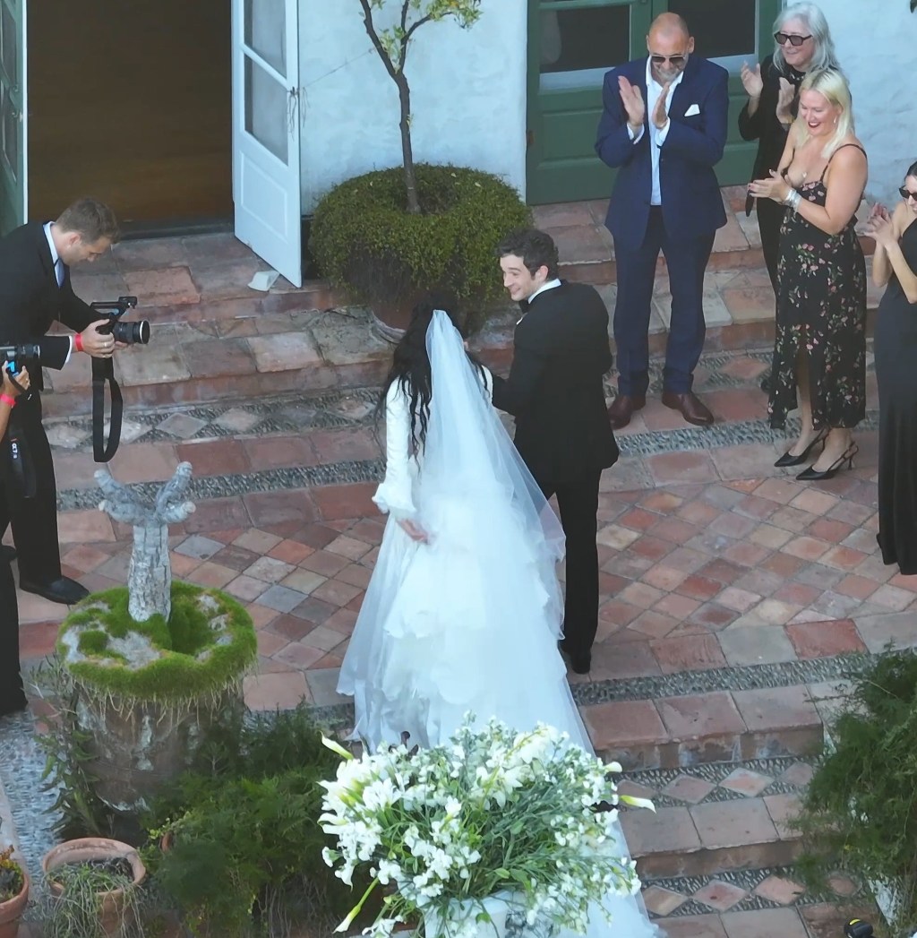 Matty Healy and Gabbriette Bechtel at their wedding, with guests applauding in the background.