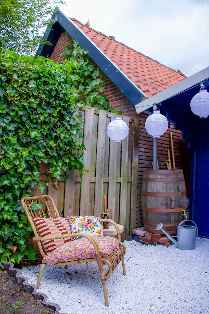 Cozy outdoor seating area with a rattan chair, colorful cushions, wooden fence, and decorative lanterns.