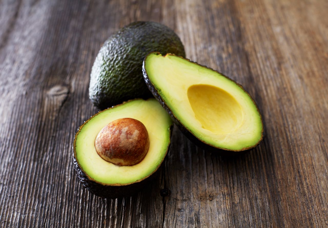 A whole avocado and two halves on a wooden surface