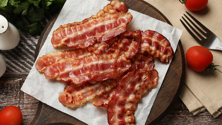 Crispy bacon displayed on a round wooden serving board, with a liner underneath the bacon.