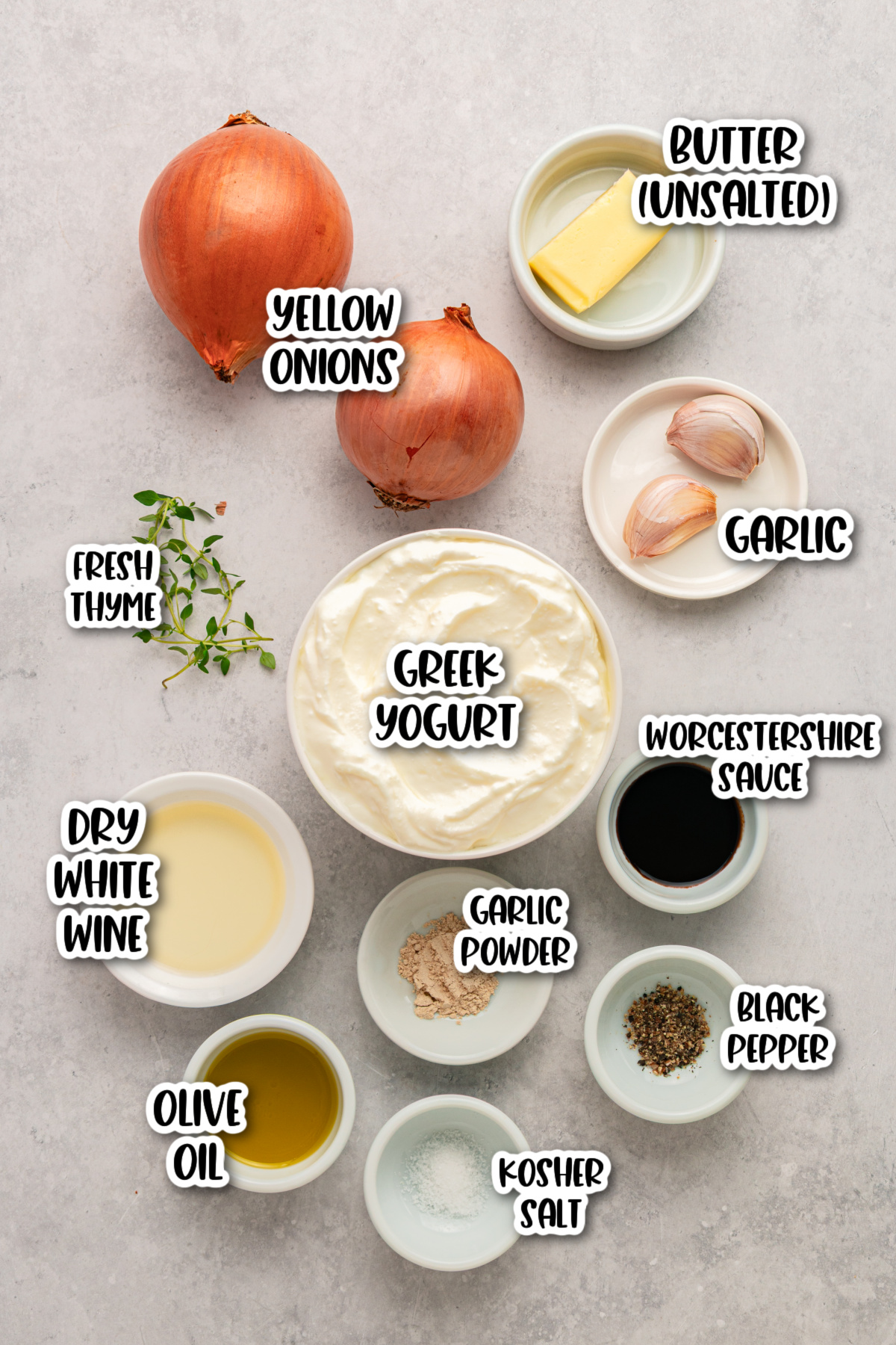Top-down view of ingredients in bowls: yellow onions, garlic, butter, fresh thyme, Greek yogurt, Worcestershire sauce, dry white wine, garlic powder, black pepper, olive oil, and kosher salt.