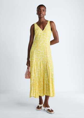 Person in a sleeveless floral maxi dress, carrying a small bag and wearing sandals, suitable for a summer look