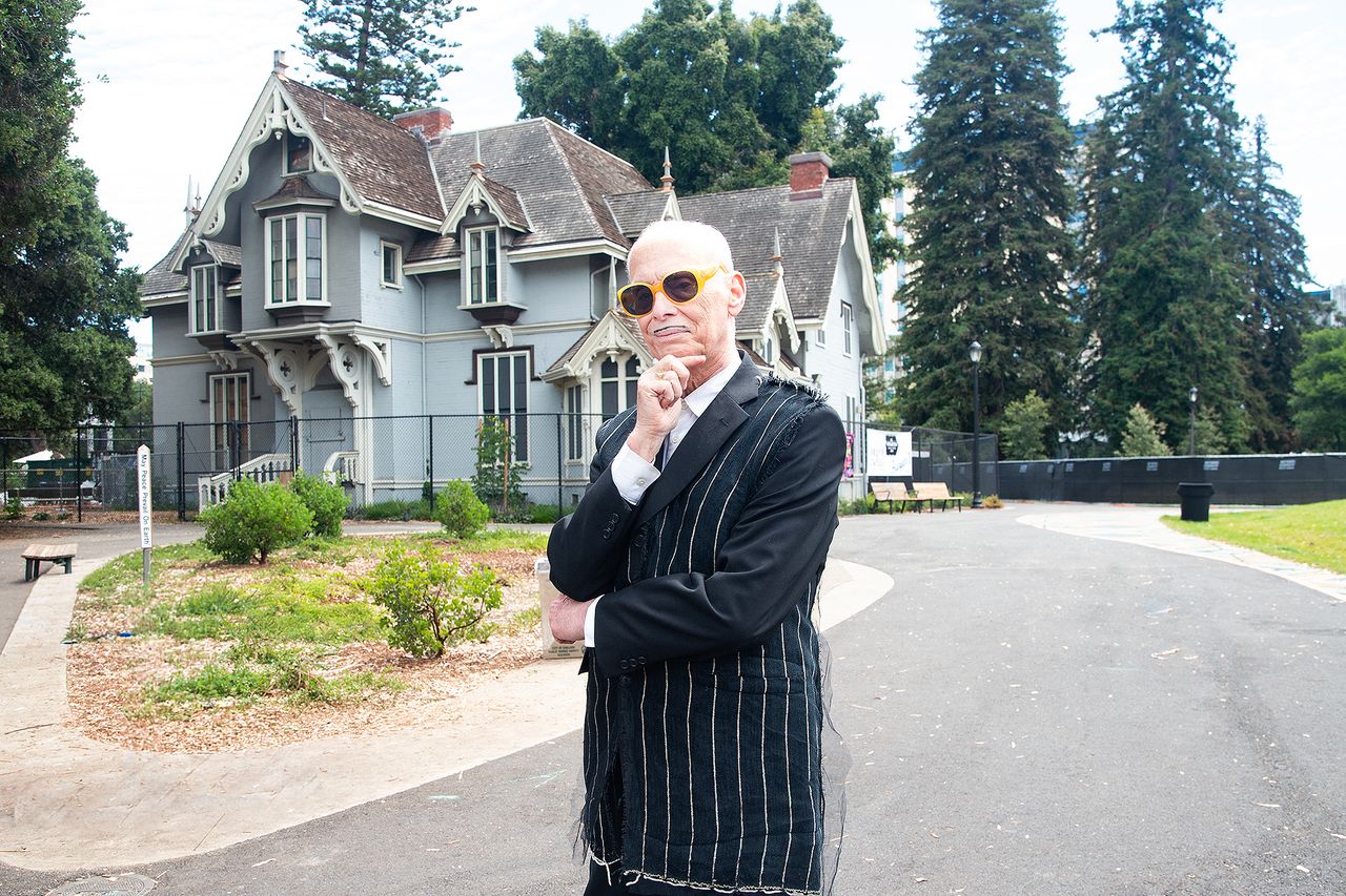 John Waters standing outdoors near a Victorianstyle house