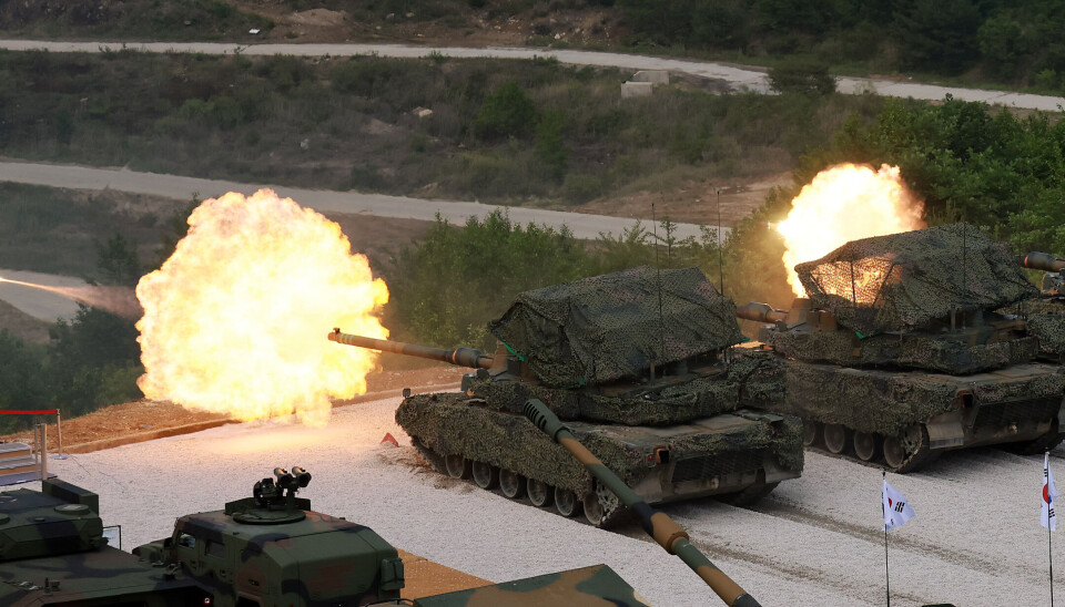 K2 tanks fire live rounds at a training range, with bright muzzle flashes and smoke.