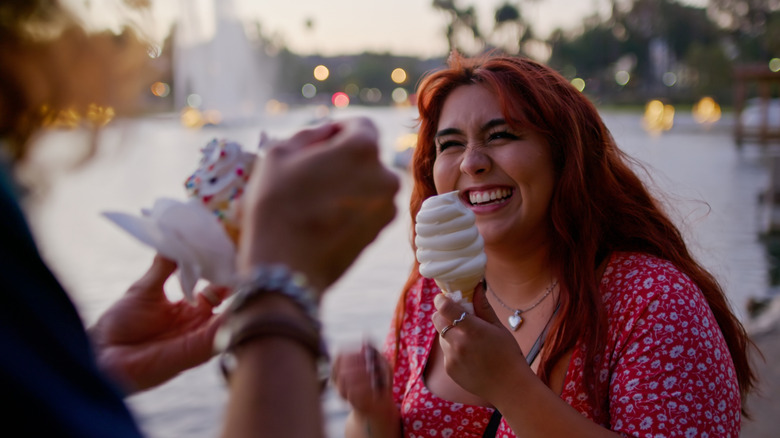 A girl eating a soft serve along with a friend who is having ice cream with sprinkles, with a river in the background.