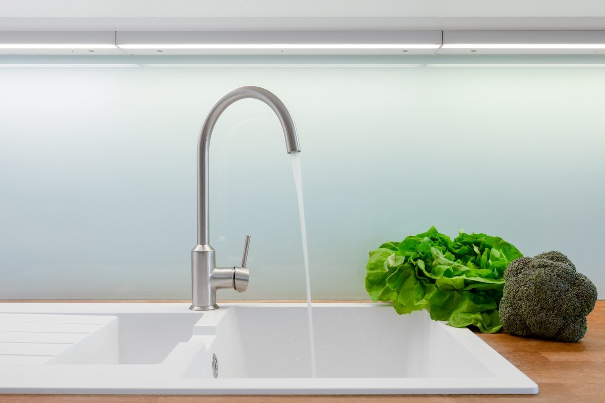 Kitchen faucet with running water with vegetables next to the sink.