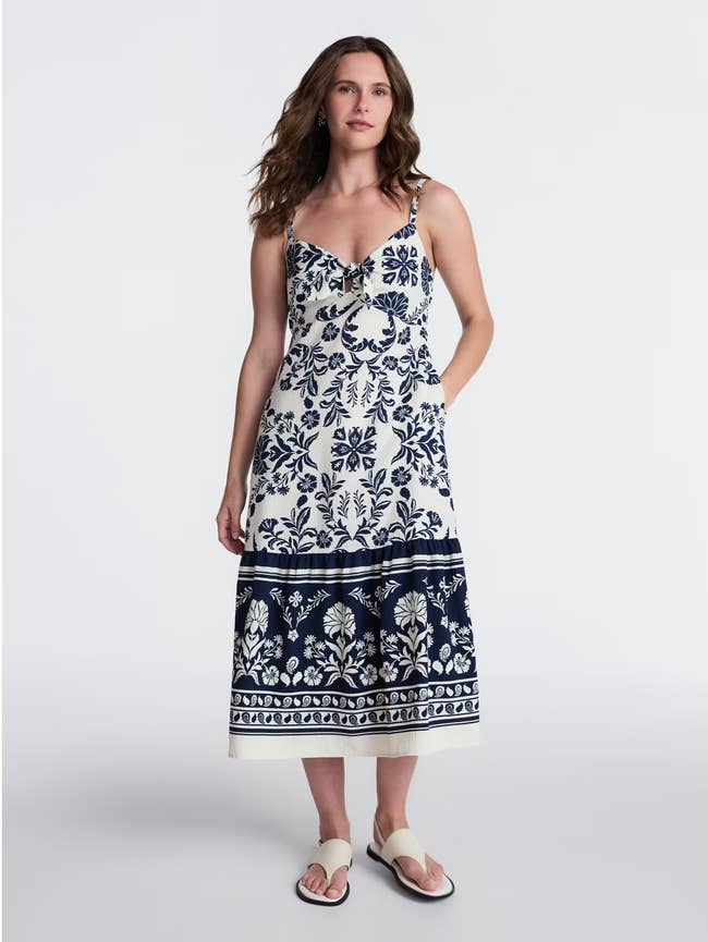 Model wearing a floral-patterned sleeveless dress and sandals, standing against a plain background