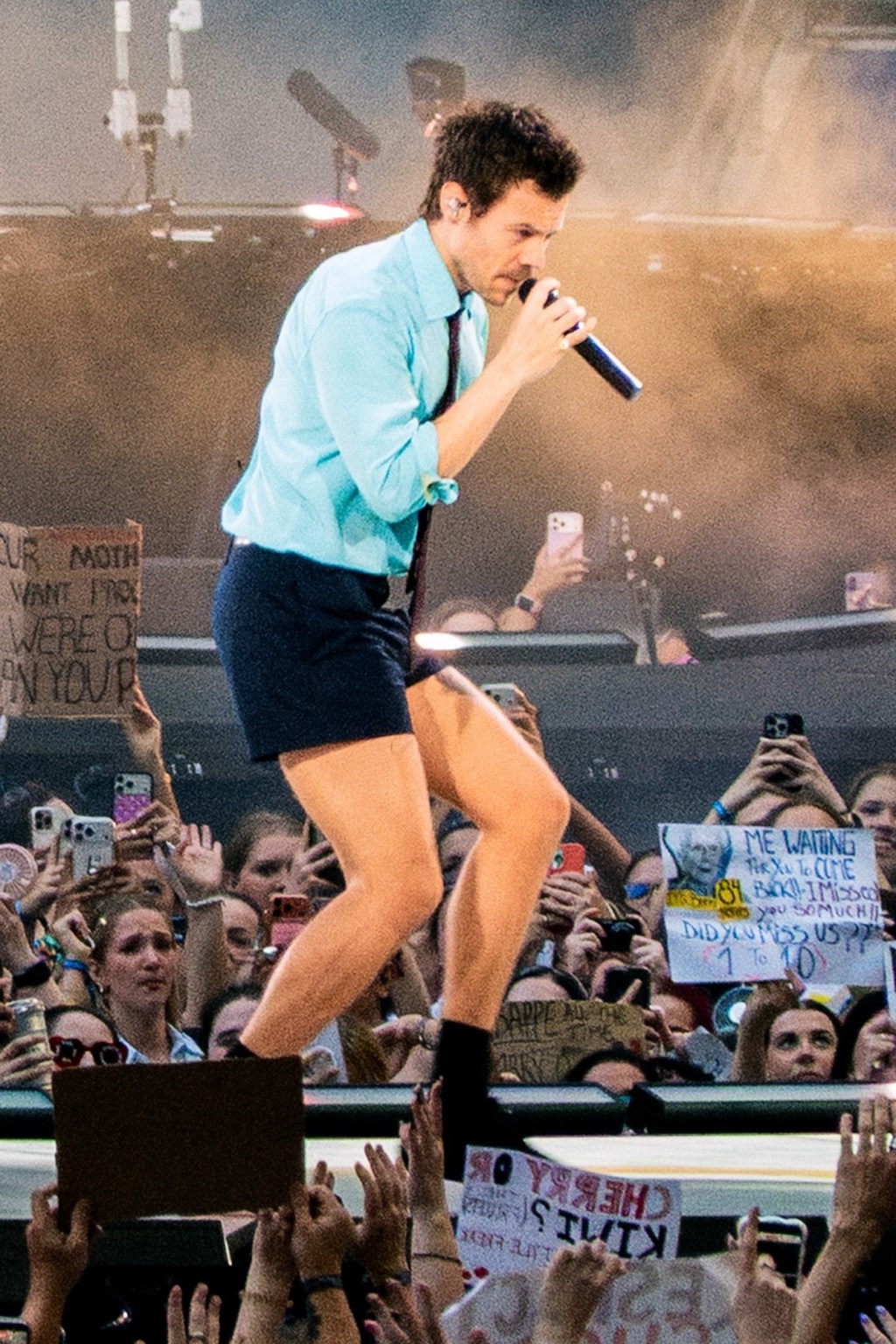 Harry Styles performing on stage at Wembley Stadium, holding a microphone.