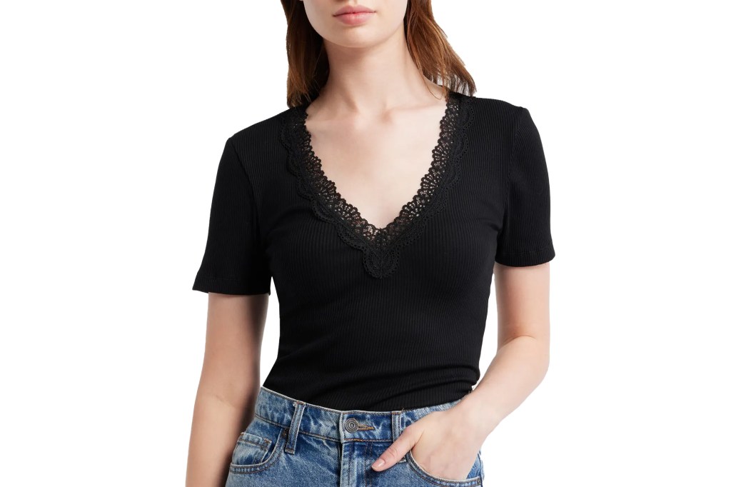 A woman wearing a black ribbed V-neck T-shirt with lace trim and blue jeans.