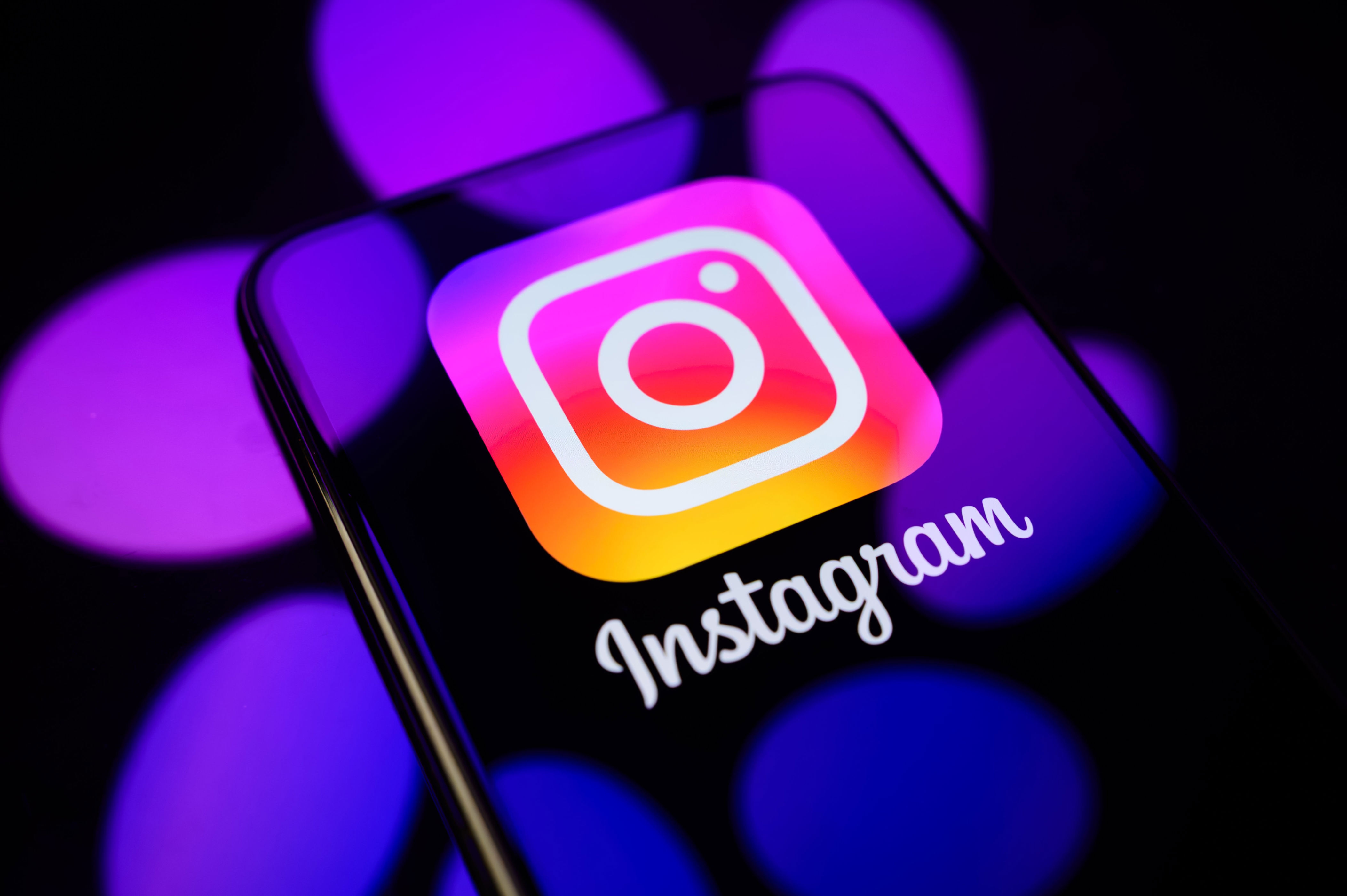 Phone displaying the Instagram logo on the screen, set against a blurred backdrop with circular light shapes