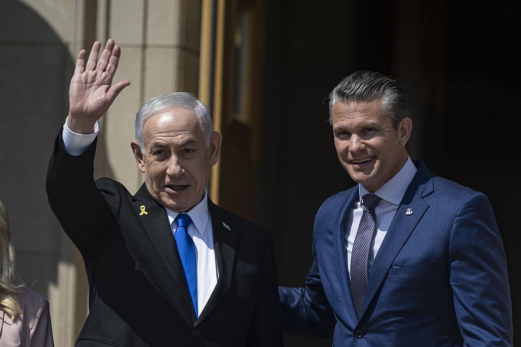 Two men in suits smiling, one waving, standing outside a building