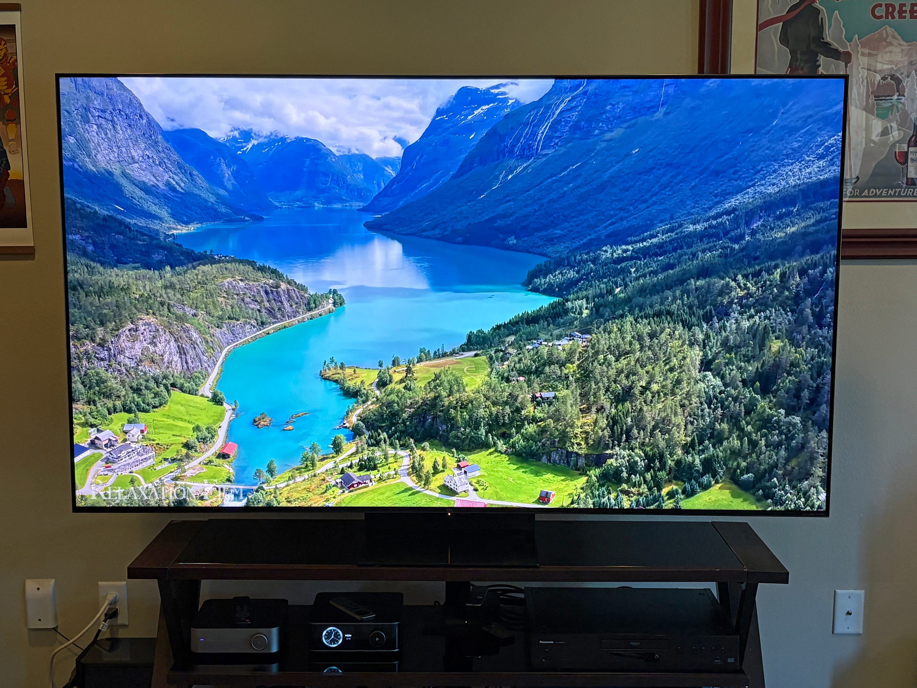 A TCL QM7L TV displays a vivid mountain lake landscape in a living room.