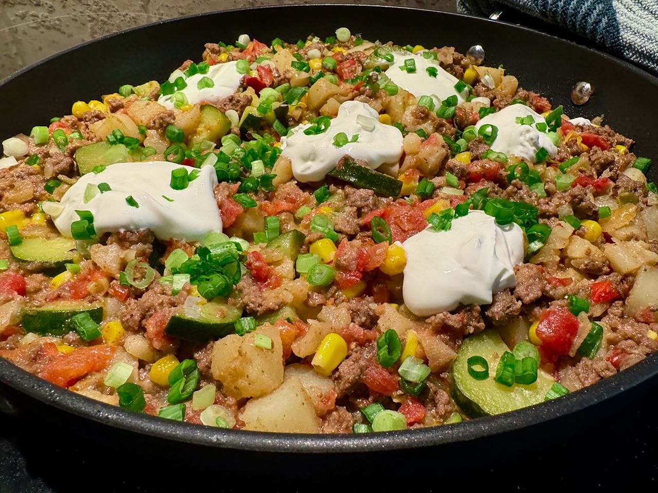skillet dinner with ground beef, potato, corn, zucchini, tomatoes dolloped with sour cream