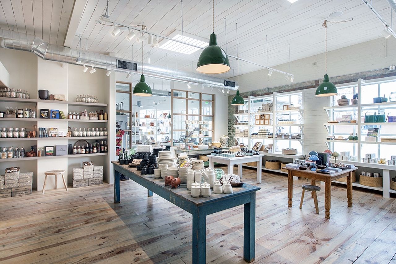 Interior of a rustic grocery shop with items displayed on tables and shelves lit by hanging lamps
