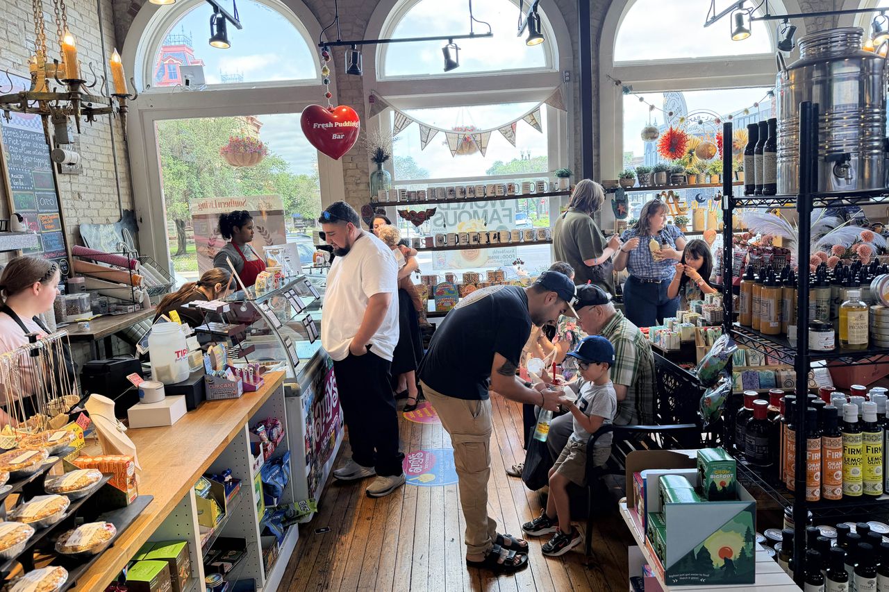 People shopping and interacting inside a small specialty grocery store with shelves of products and a counter