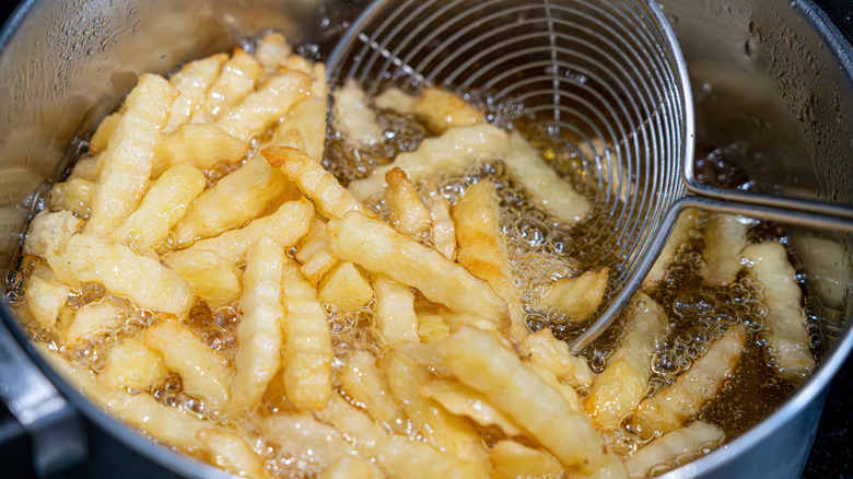 Potatoes in boiling oil, homemade french fries, deep fried potato cooking in metal fryer pot