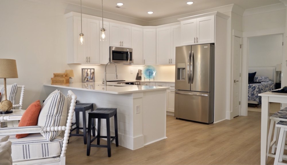 A suite of stainless steel appliances are embedded in an L-shaped formation of white cabinetry inside the kitchen.