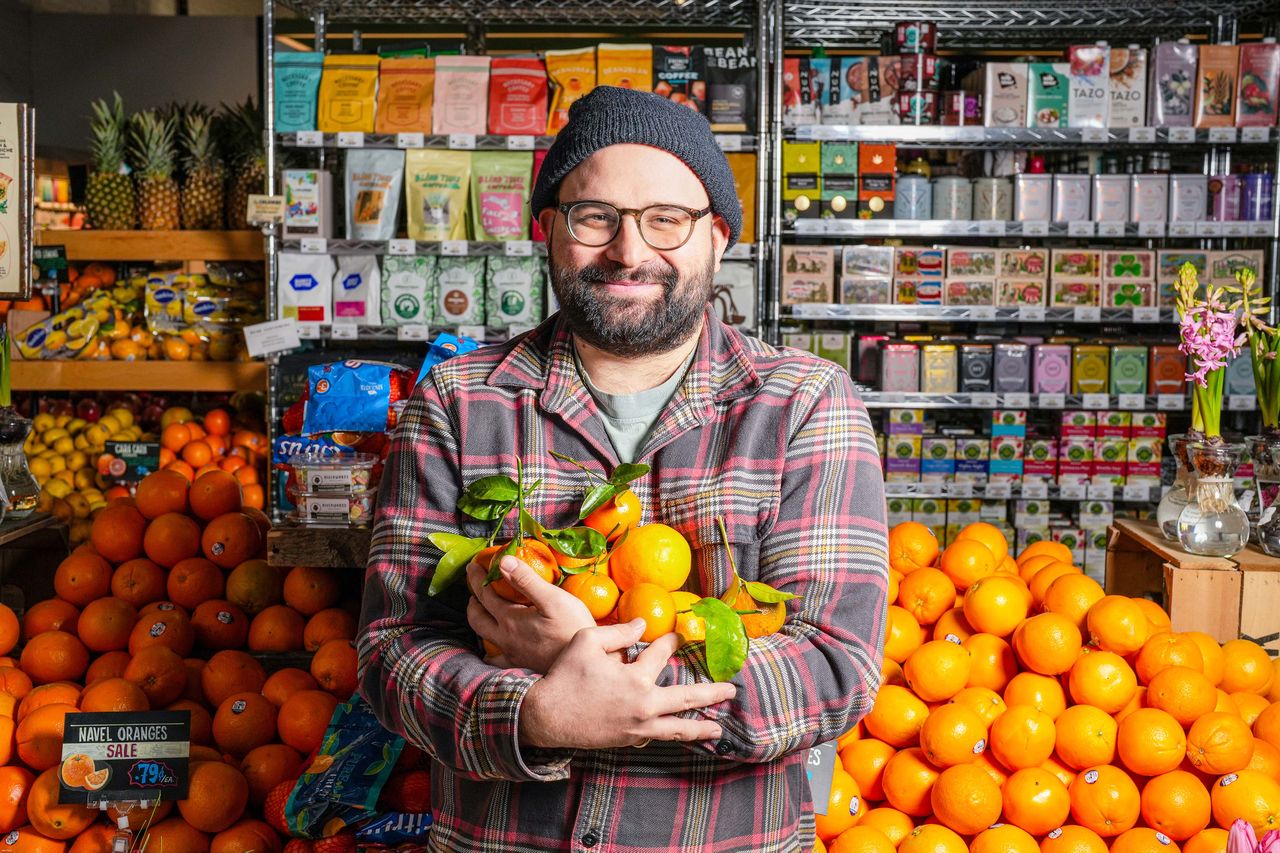 A person holding oranges standing in a grocery produce section with shelves in the background