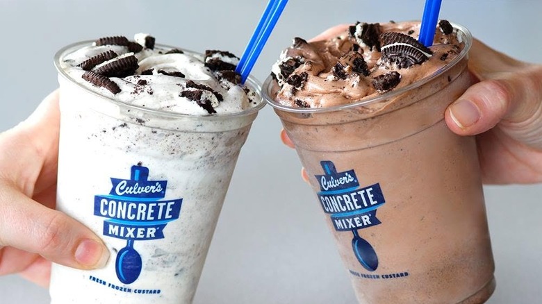 Two people holding up the vanilla Oreo and chocolate Oreo Culver's concrete mixer against a grey background.