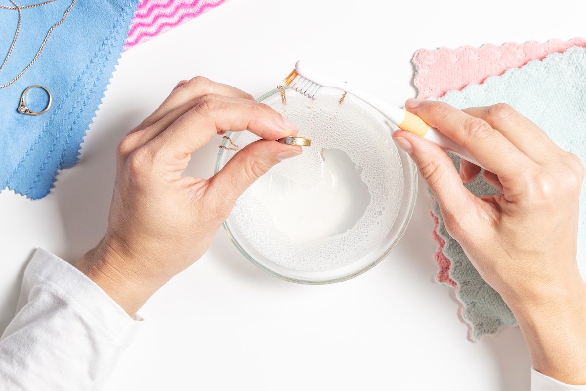A person uses rubbing alcohol, a brush, and cloth to clean jewelry.