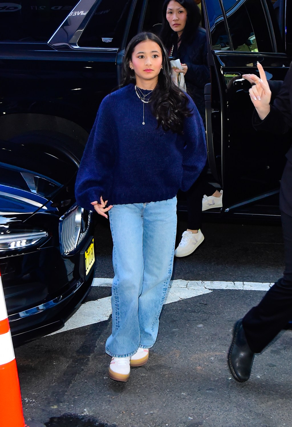 Kaylee Hottle, a young woman, in a navy blue sweater and light blue jeans, walking outside a building.