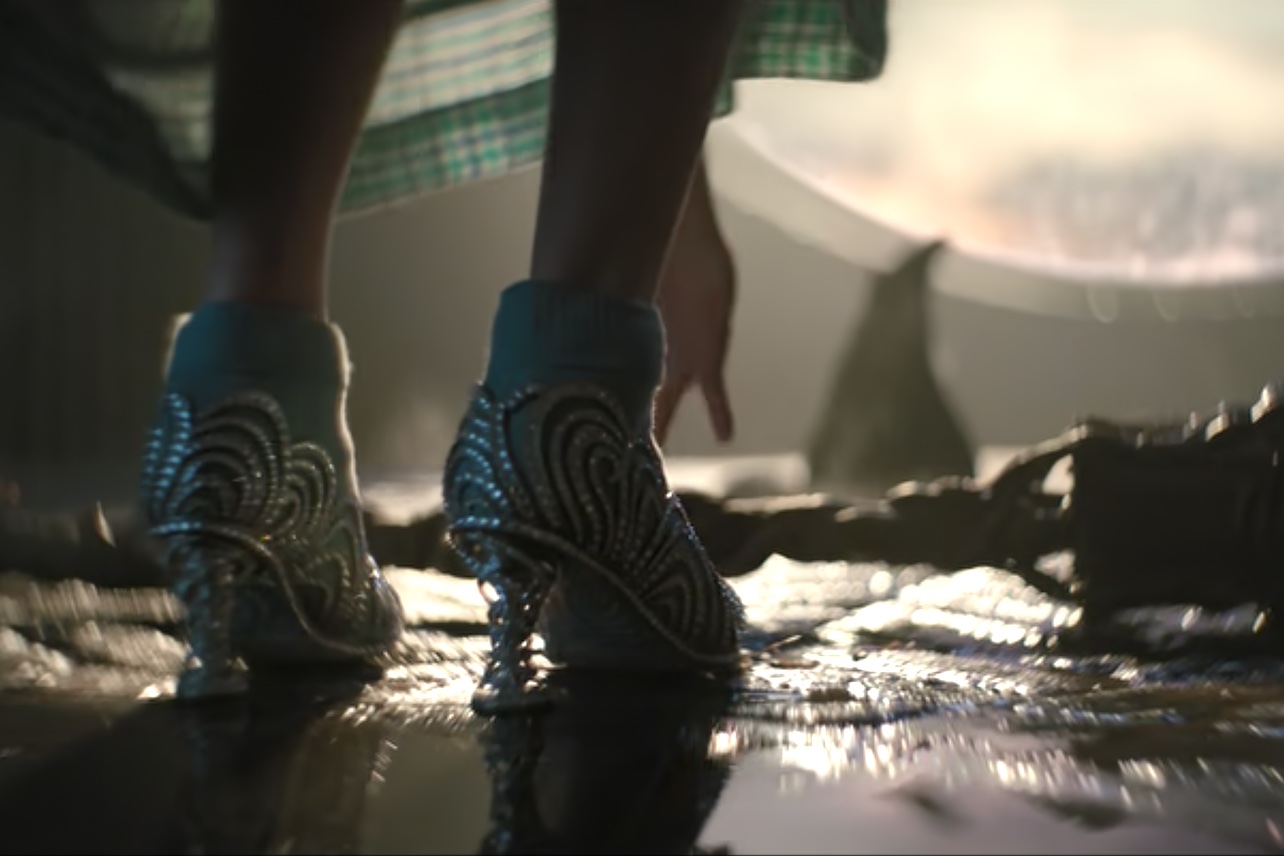 Person wearing elaborate, patterned shoes with high heels walking on a reflective surface.