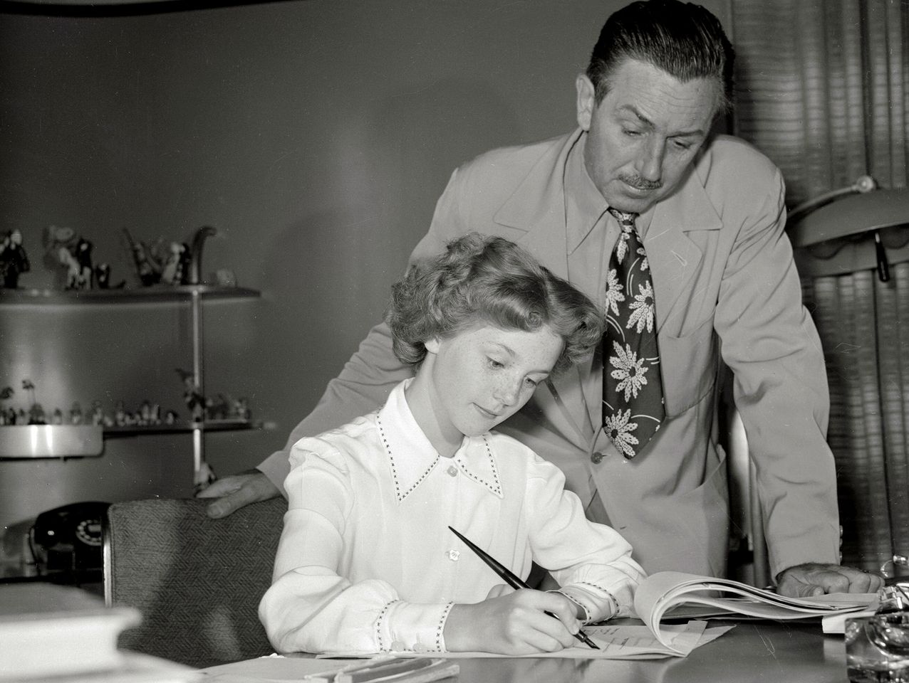 Walt Disney looks on as 11-year-old Kathryn Beaumon signs a contract to act as the voice of Alice in Wonderland