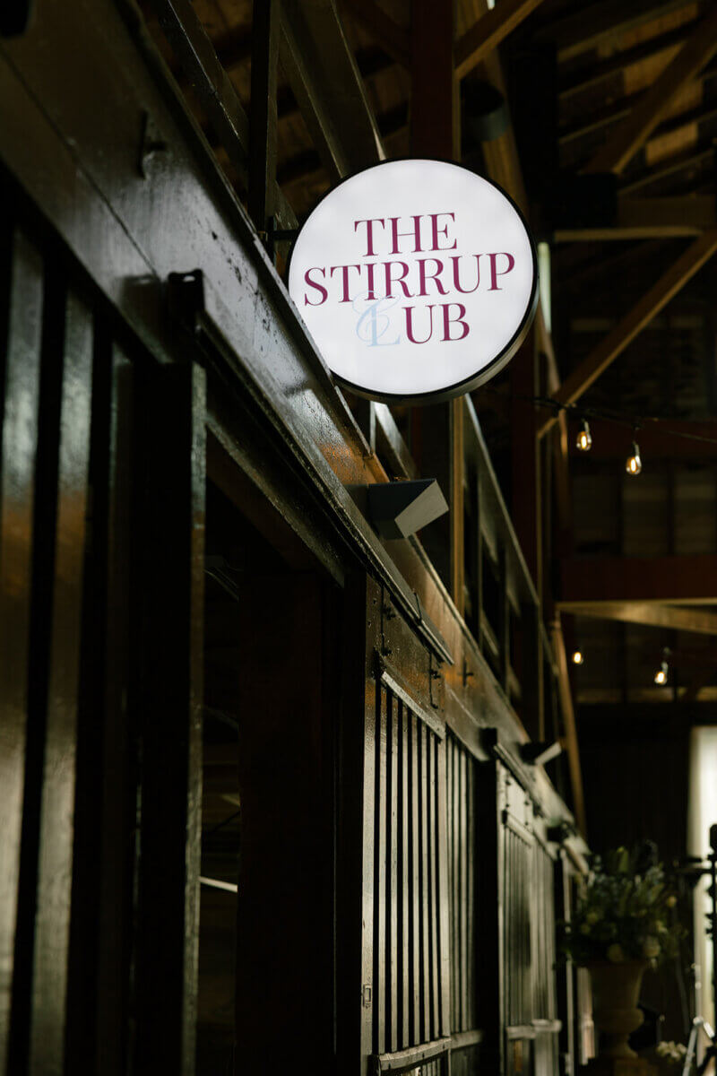 For the wedding, they designed “The Stirrup Club” bar in one of the horse stalls, complete with lounge furniture, a café light above the stall, and a brass antique horse with fringe from the 1700s. Image: Rachel Fugate Photography
