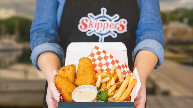 Employee holding Skippers seafood basket with fried fish, tarter sauce, and fries