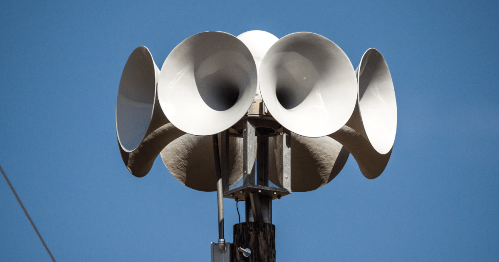 Outdoor emergency tornado warning siren against a clear blue sky in a local community.