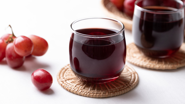 Two glasses of grape juice sitting on coasters surrounded by grapes