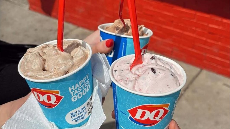 A group of three people taking pictures with their individual cups of Dairy Queen Blizzard in front of the shop.